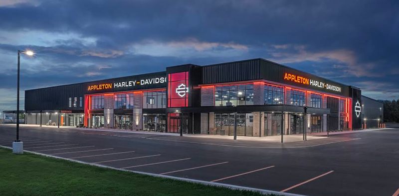 Exterior of the Appleton Harley-Davidson dealership at dusk, with illuminated branding and glazed showroom frontage